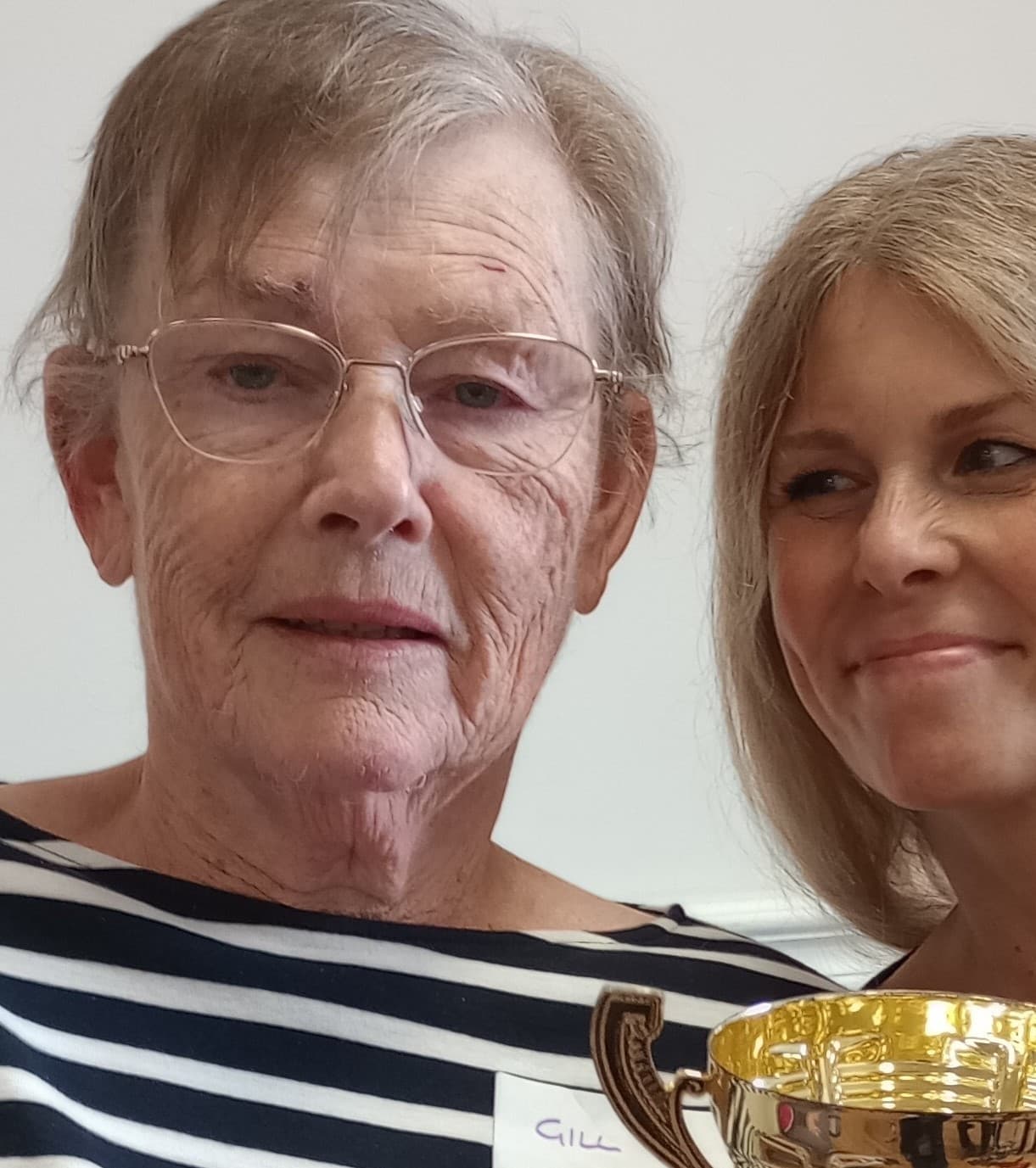 Two people smiling; one holds a gold trophy. - Home Instead