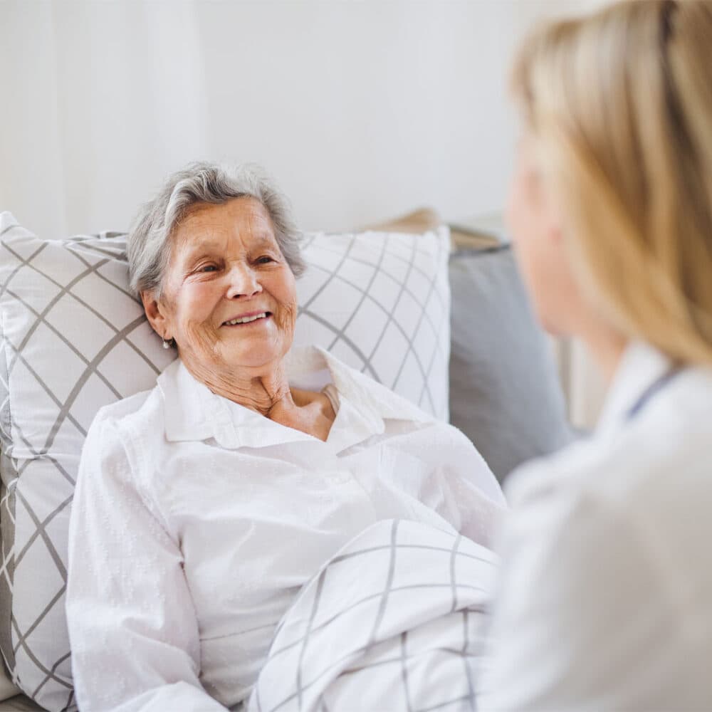 care professional sat on the end of the bed talking to her client in bed