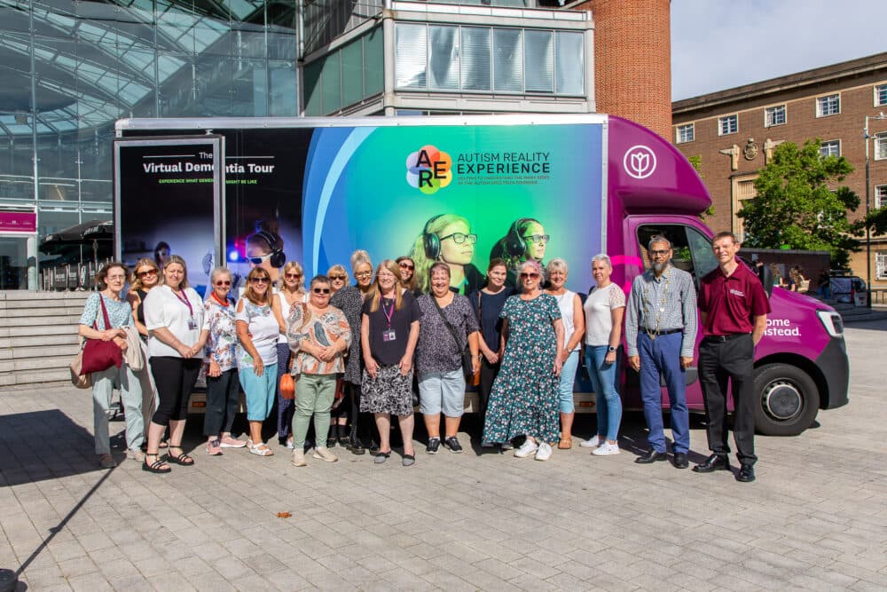 A group of people stands in front of a colorful Autism Reality Experience truck. - Home Instead