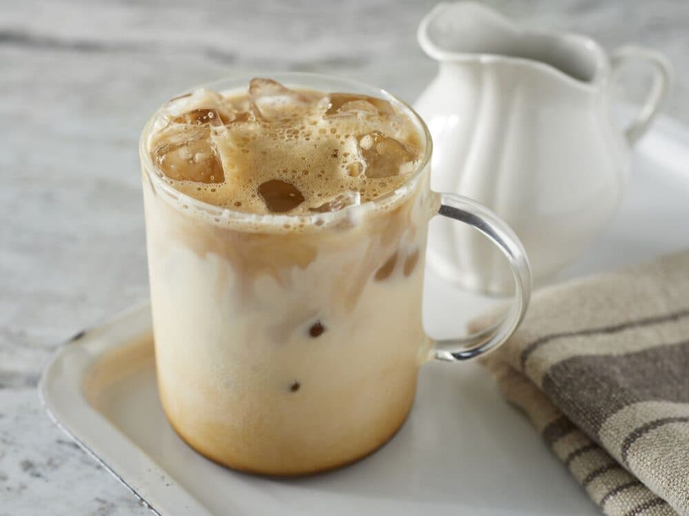 Iced coffee in a clear mug on a tray with a small jug and a cloth napkin. - Home Instead