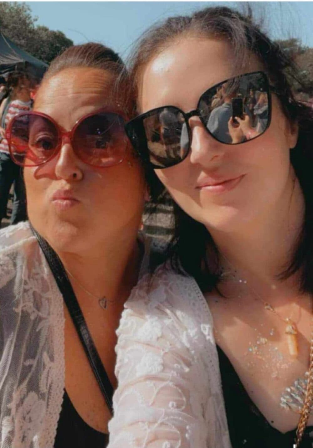 Two women wearing sunglasses smile for a selfie outdoors on a sunny day. - Home Instead
