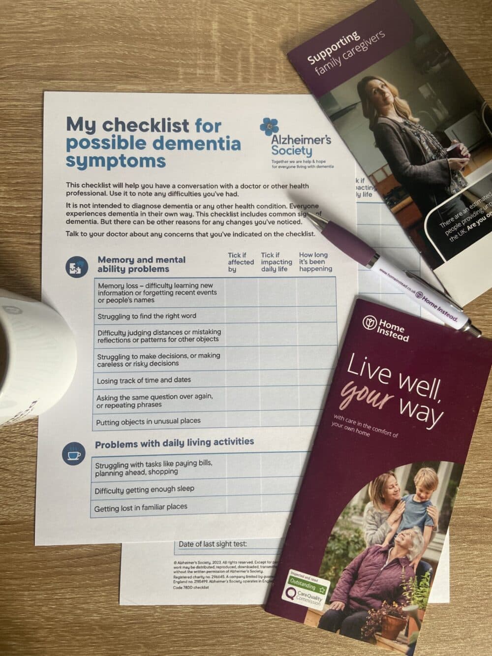 Picture of the Dementia Checklist flat on a table, with a Home Instead pen, Home Instead care leaflets and a coffee mug beside.