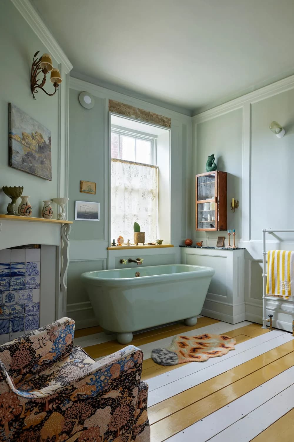 Vintage-style bathroom with a green bathtub, patterned armchair, striped rug, and art on the walls. - Home Instead