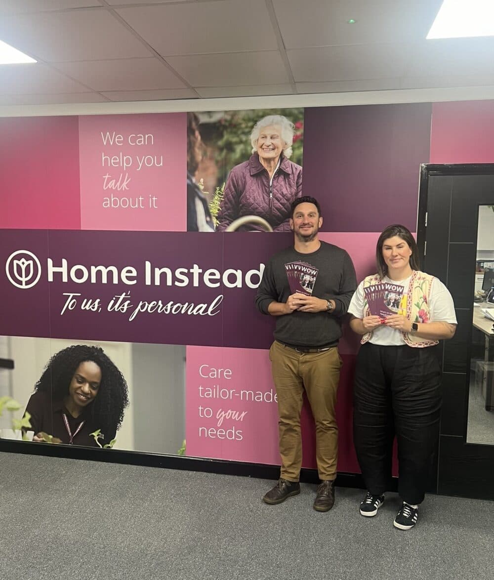 Image of two people stood against a wall holding up WOW Guides.