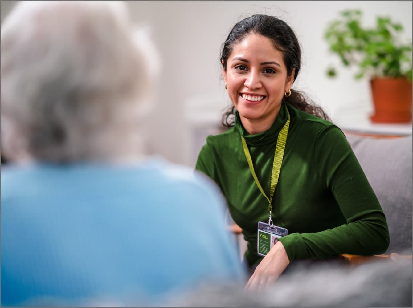 A woman in a green top smiles while sitting across from an older person in a blue top. - Home Instead Dementia Care in Ballygally