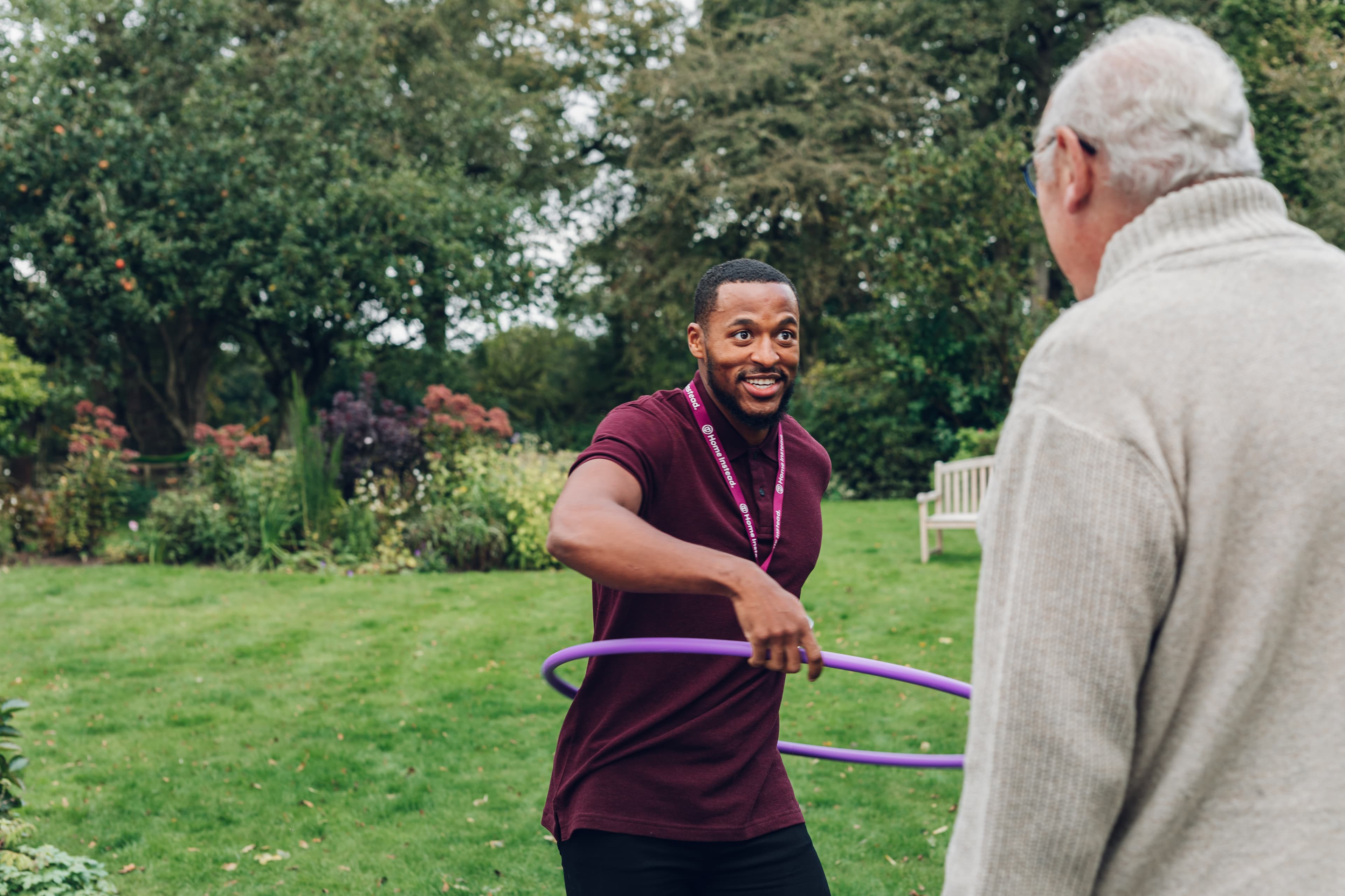 Image of a male care professional in the garden alongside an older male. They are enjoying the outdoors an light exercise.