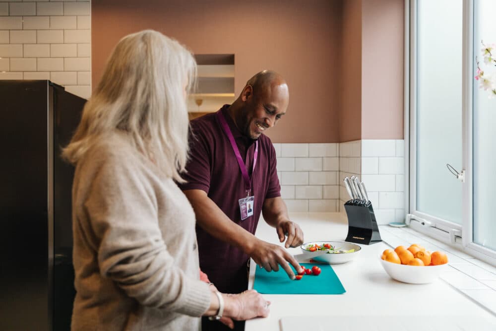 Two people preparing food in a kitchen, man cutting vegetables, woman watching. - Home Instead