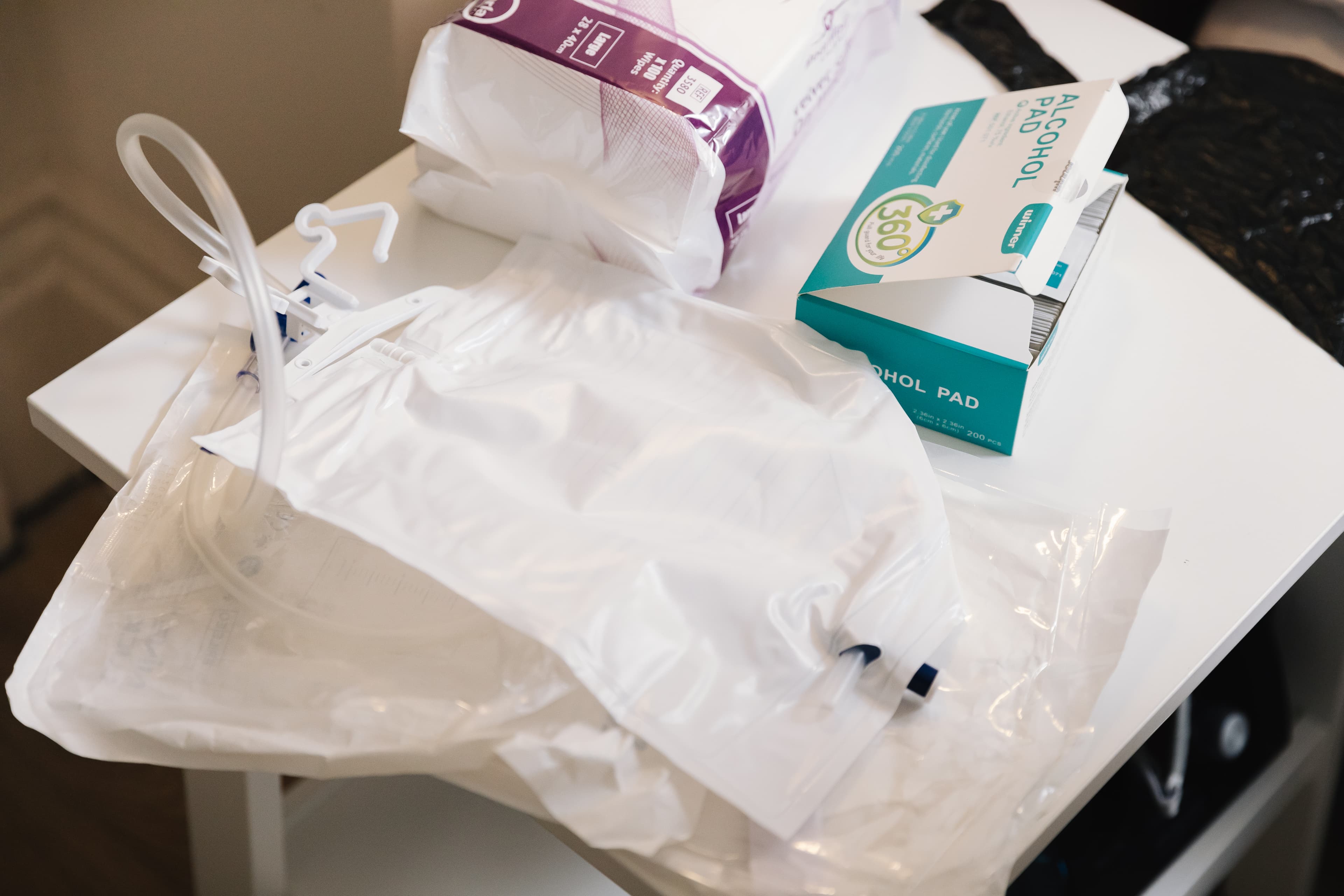 Medical supplies, including a colostomy bag, alcohol pads, and a package, on a white table. - Home Instead