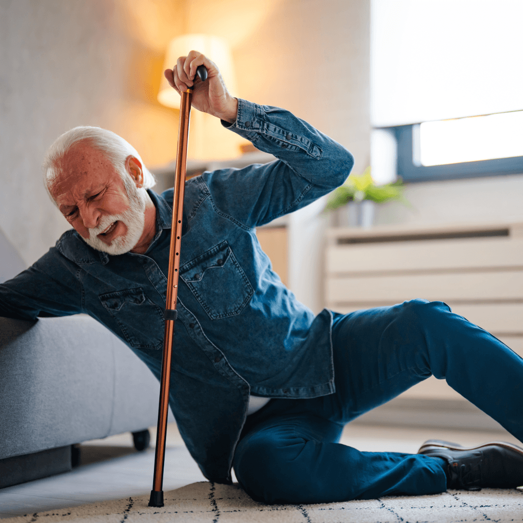 Older man in distress on the floor, clutching a cane and trying to get up next to a couch. - Home Instead
