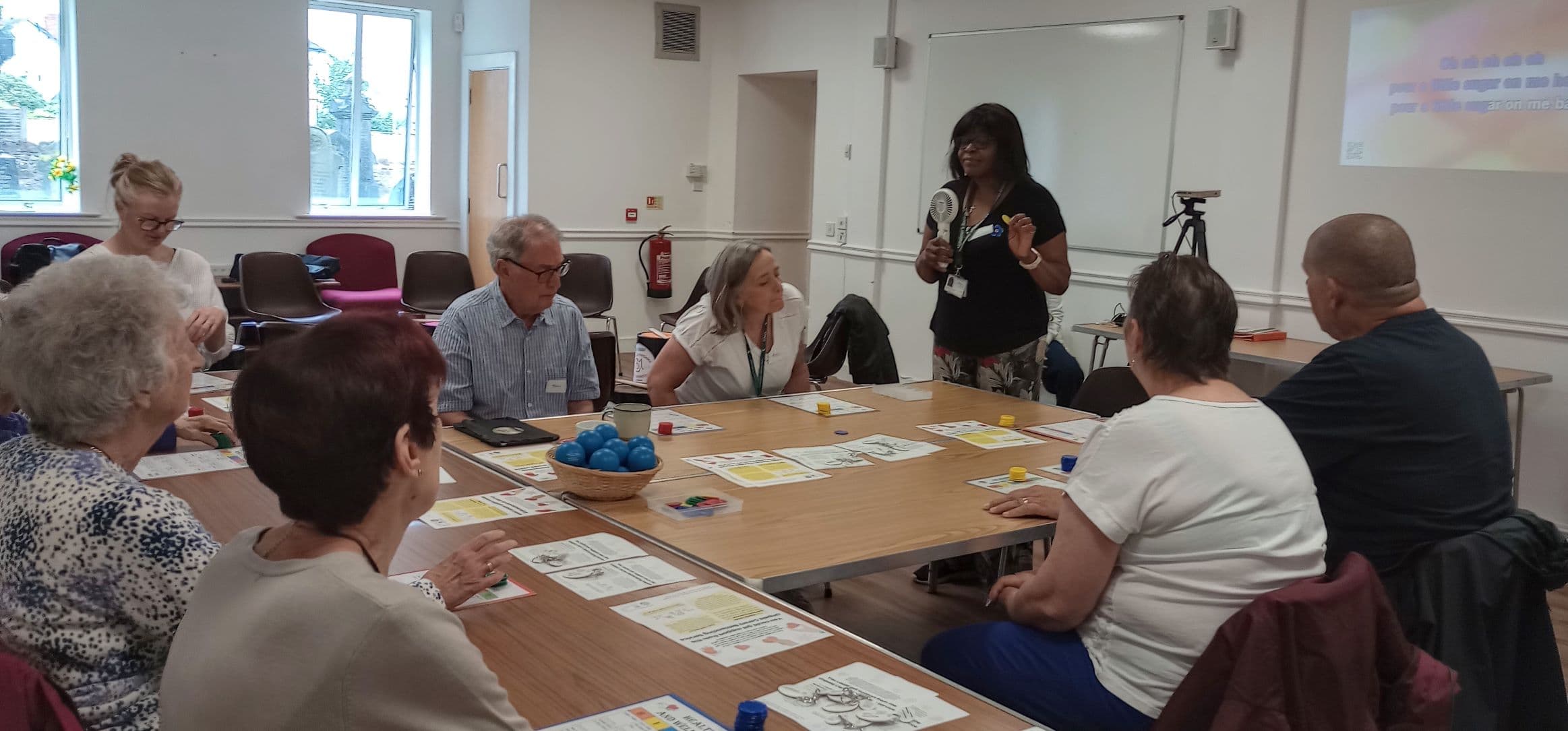 A group of people sitting around a table listening to a person speaking in a classroom setting. - Home Instead