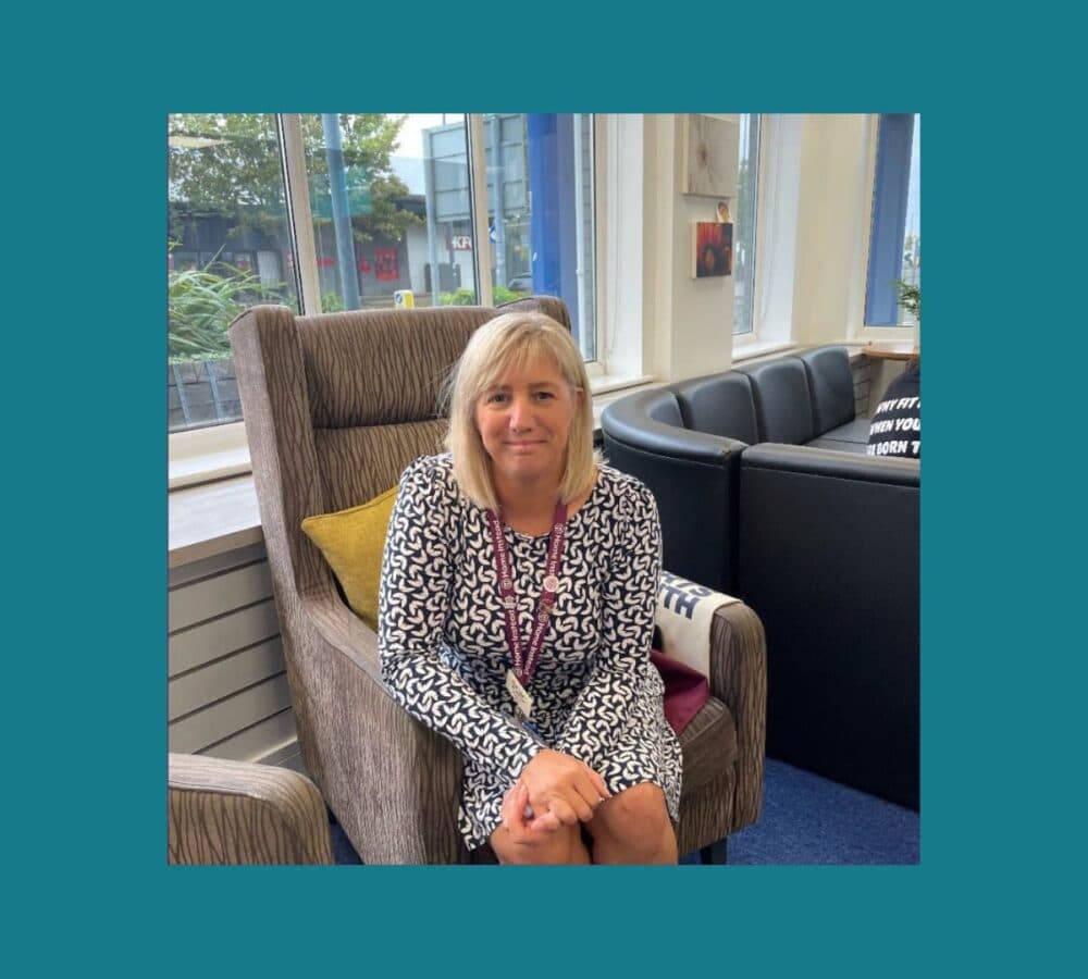 Helen Brown smiling and wearing a dress, sitting on a gray couch at Spark Community Space