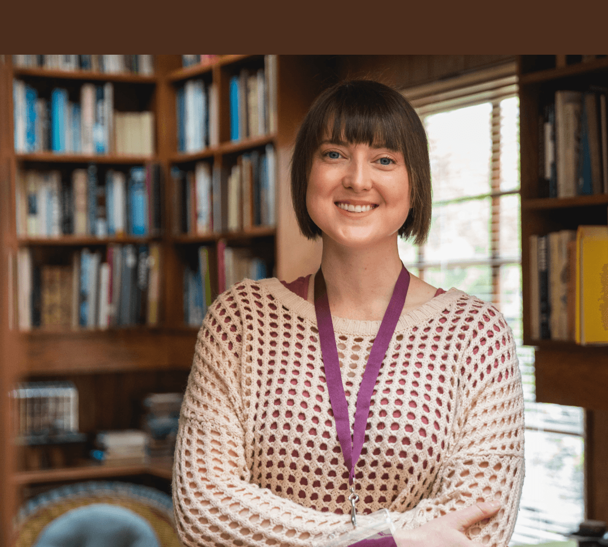 A young Care Professional standing with short black hair inside the house with books in the background