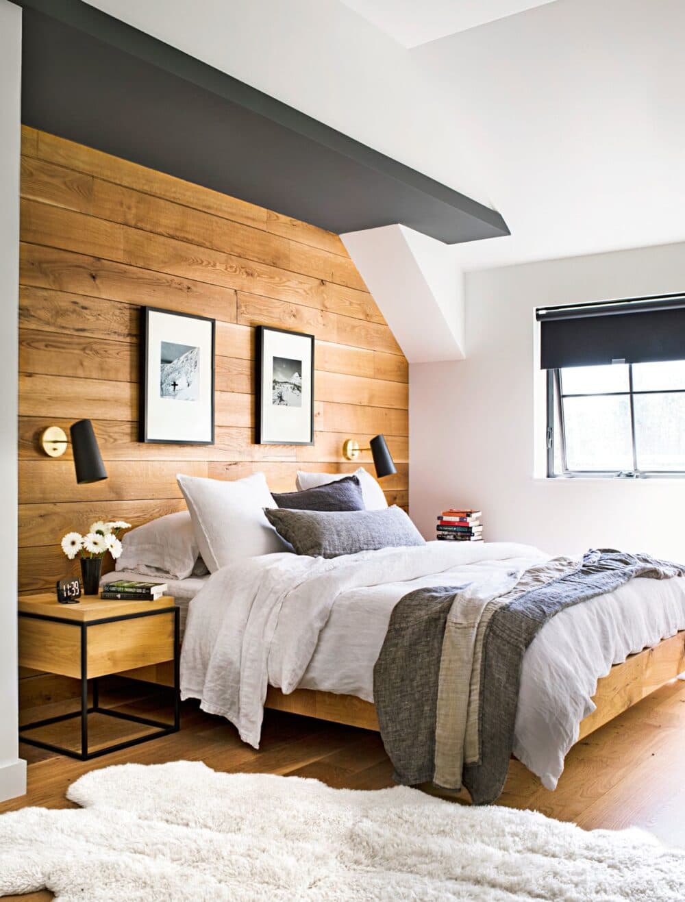 A cozy bedroom with a wooden accent wall, bed with grey and white bedding, side table, and two framed photos. - Home Instead