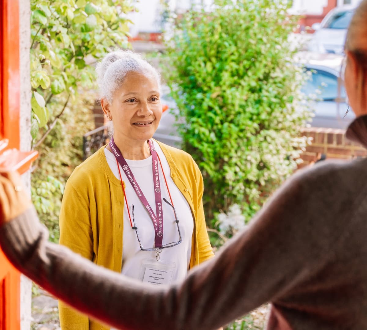 Care Professional wearing mustard sweatshirt at the door of her client house