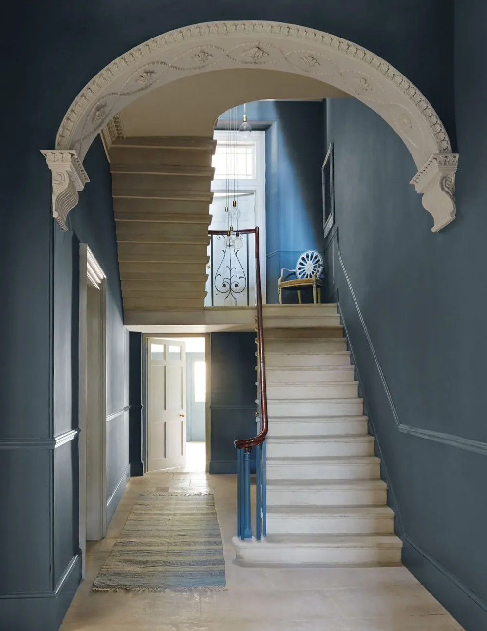 Elegant staircase with blue walls, ornate archway, and wooden handrail in a well-lit hallway. - Home Instead