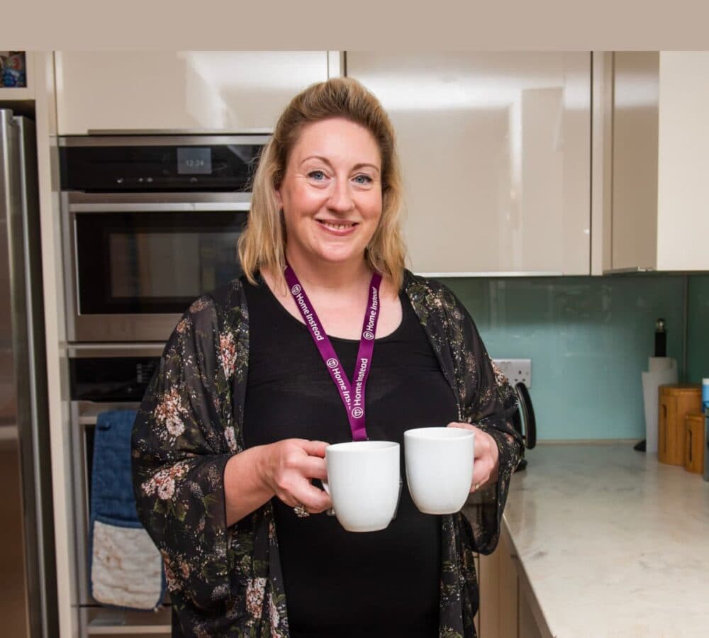 A woman in the kitchen wearing black. smiling while holding two white cups