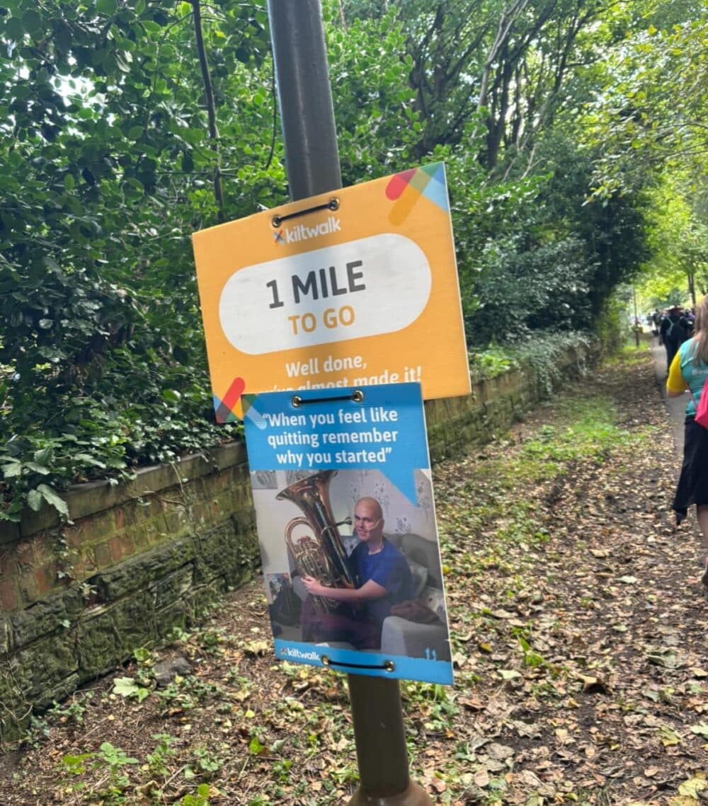 Signs on a forest trail: "1 Mile to Go" and a motivational poster encouraging perseverance. - Home Instead