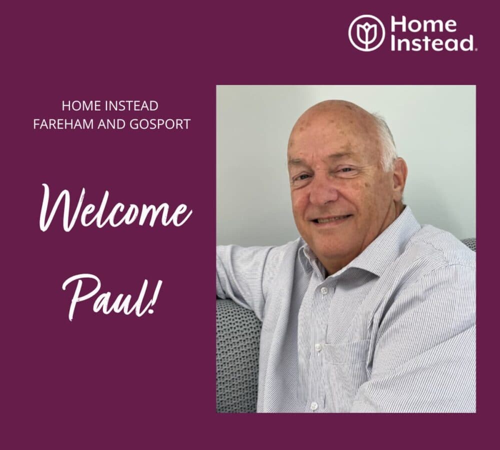 An old man smiling with white hair and wearing long sleeves while sitting on a couch