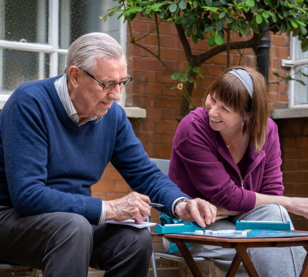 A Senior man playing Scrabble and talking with his carer outside his house