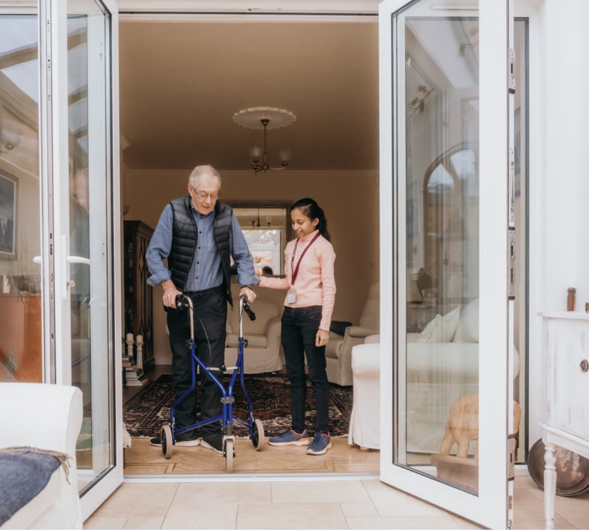 Senior man with his carer walking happily at the side of the road with cars parked and green grass along the path
