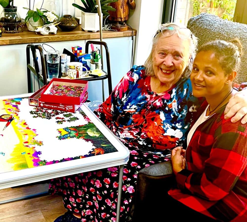 Senior woman in her home with her carer doing jigsaw puzzles and having a great time together