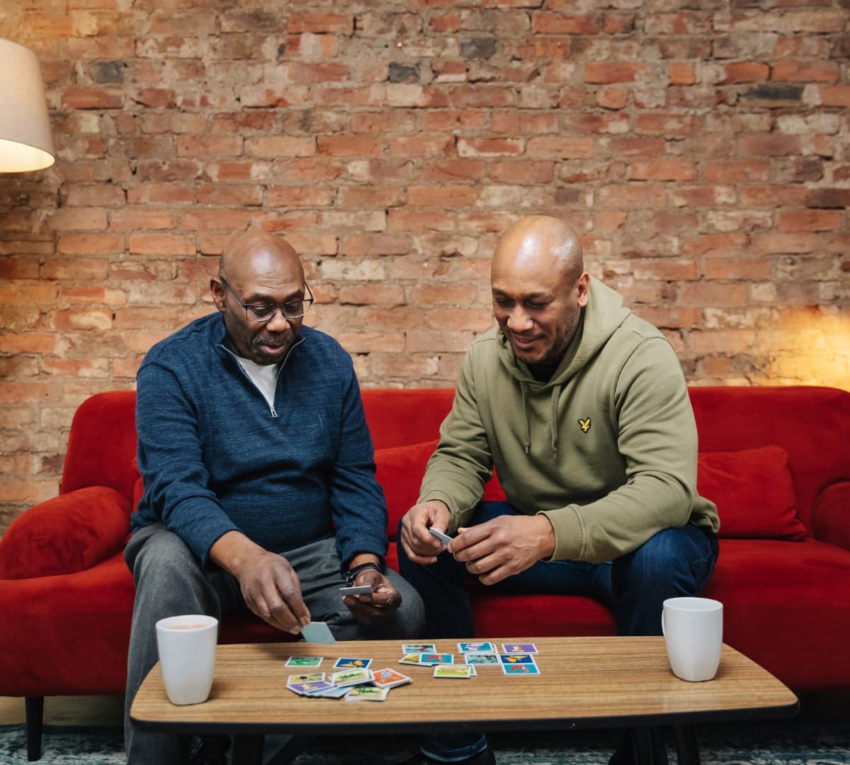 A Father and son playing puzzles, sitting at a red couch, both are happy and enjoying each other's company.