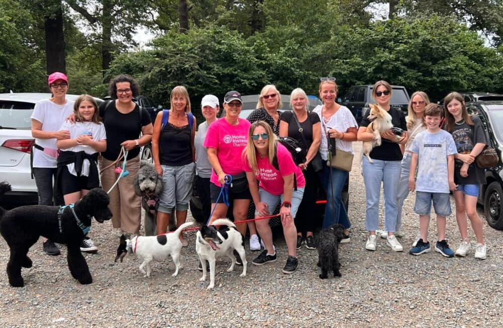 Group of people with dogs posing outdoors in a parking lot, surrounded by trees. - Home Instead
