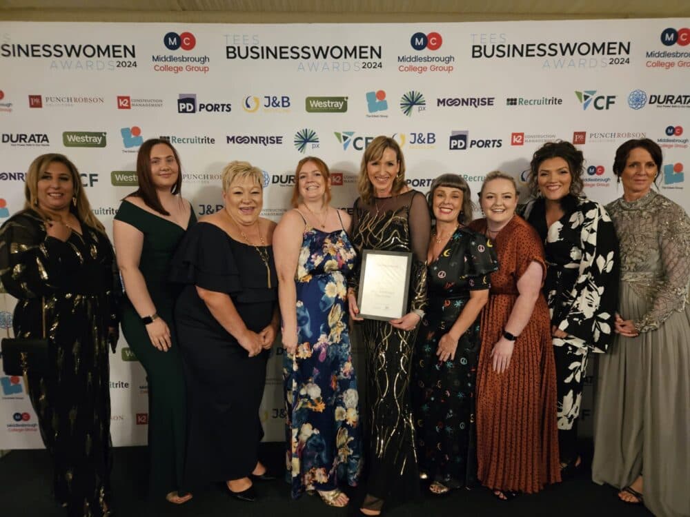 A group of women posing together at an awards event, one holding a framed certificate. - Home Instead