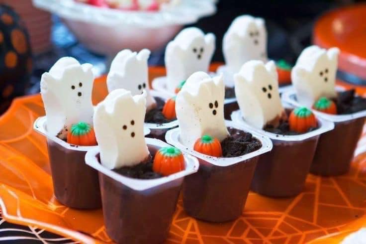 Chocolate pudding cups topped with marshmallow ghosts and candy pumpkins on an orange tray. - Home Instead
