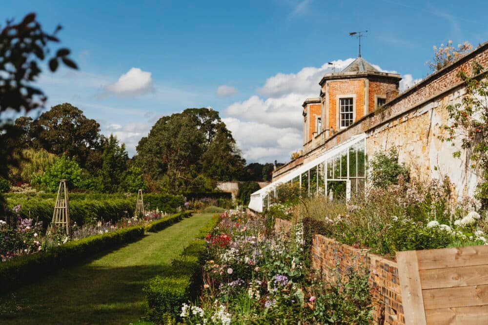Historic brick building with a lush garden, lawn pathway, and a sunny sky. - Home Instead
