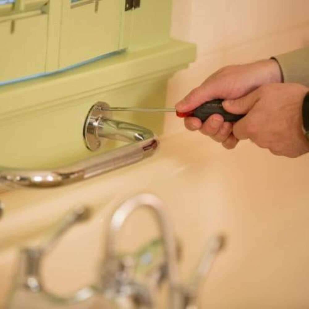A person uses a screwdriver to install a metal grab bar near a bathroom sink. - Home Instead