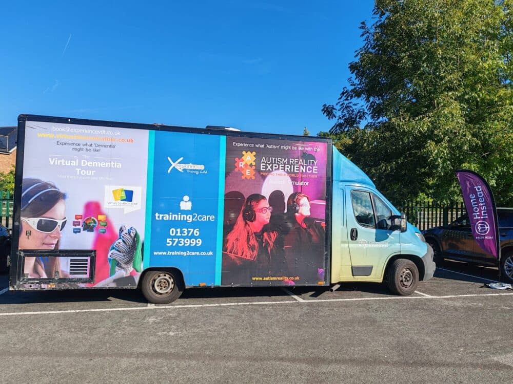 A van advertising a Virtual Dementia Tour and Autism Reality Experience, parked in a sunny lot. - Home Instead