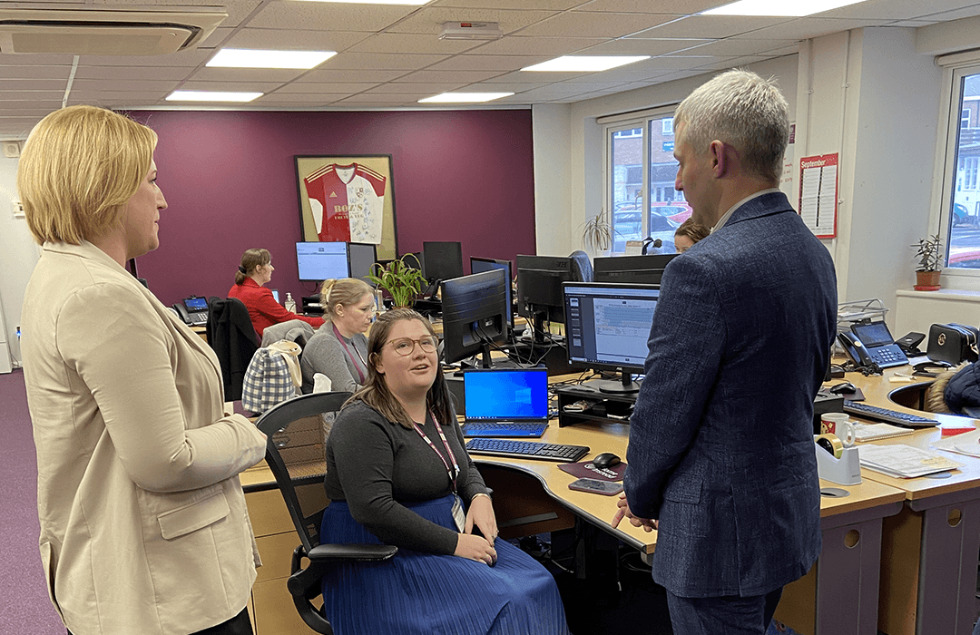 Male MP for Woking stood chatting to lady sat down on chair and lady stood up introducing them in office setting