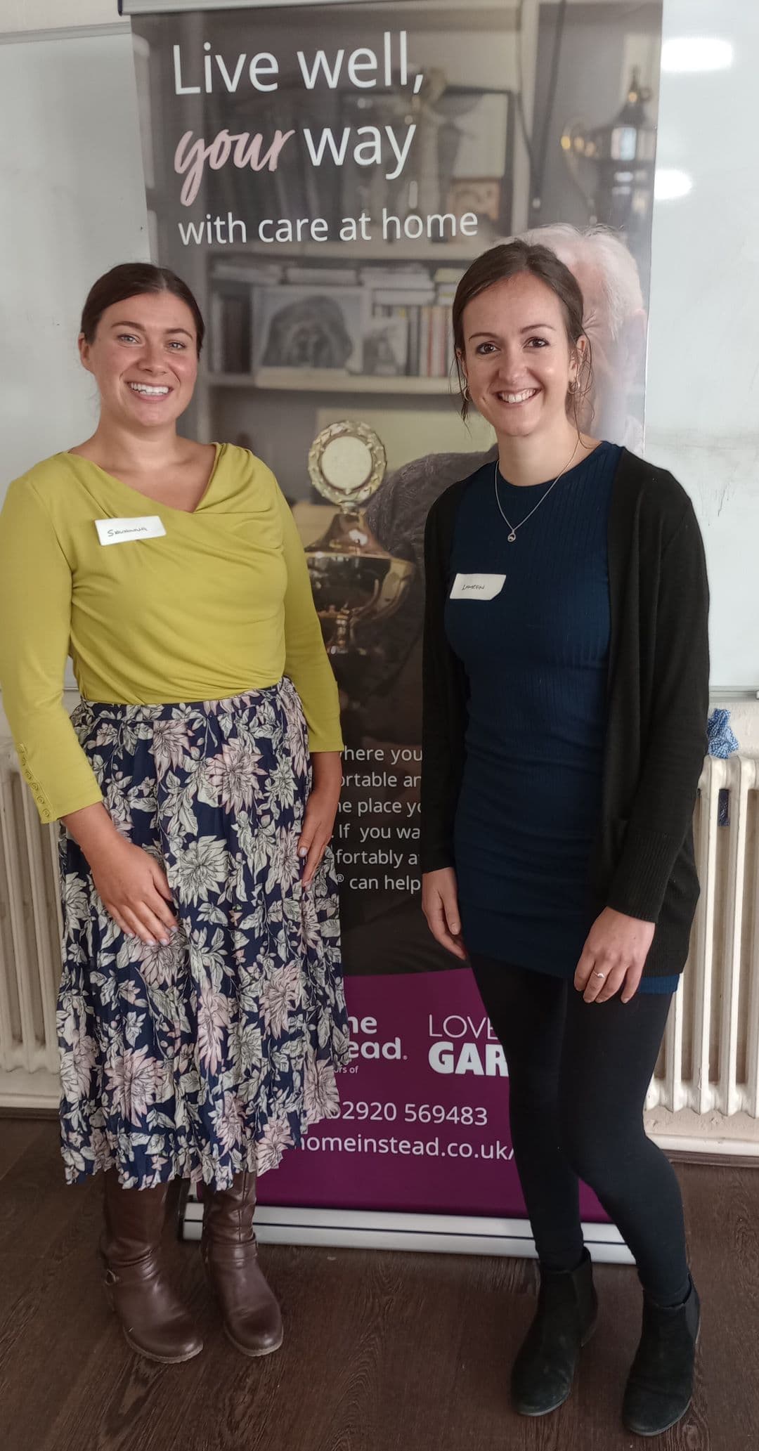 Two people smiling in front of a banner about home care services. - Home Instead