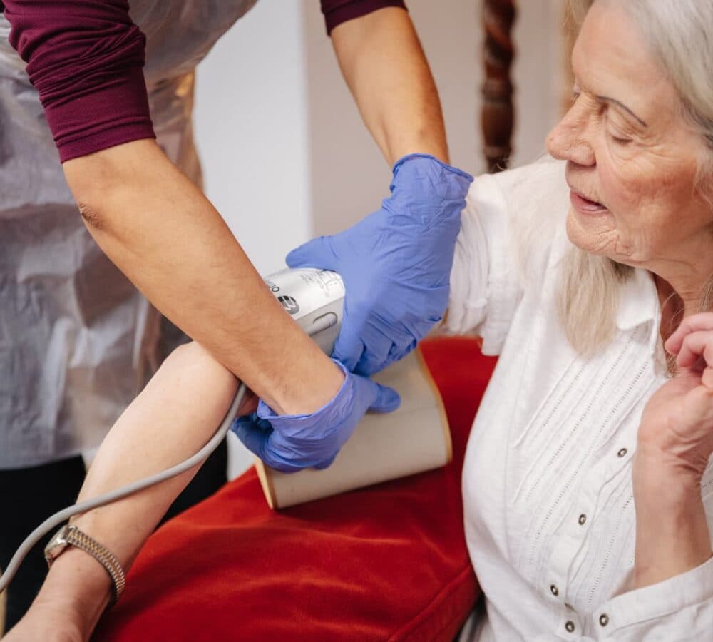 Senior woman wearing white top being cared for by her carer wearing gloves and taking her blood pressure