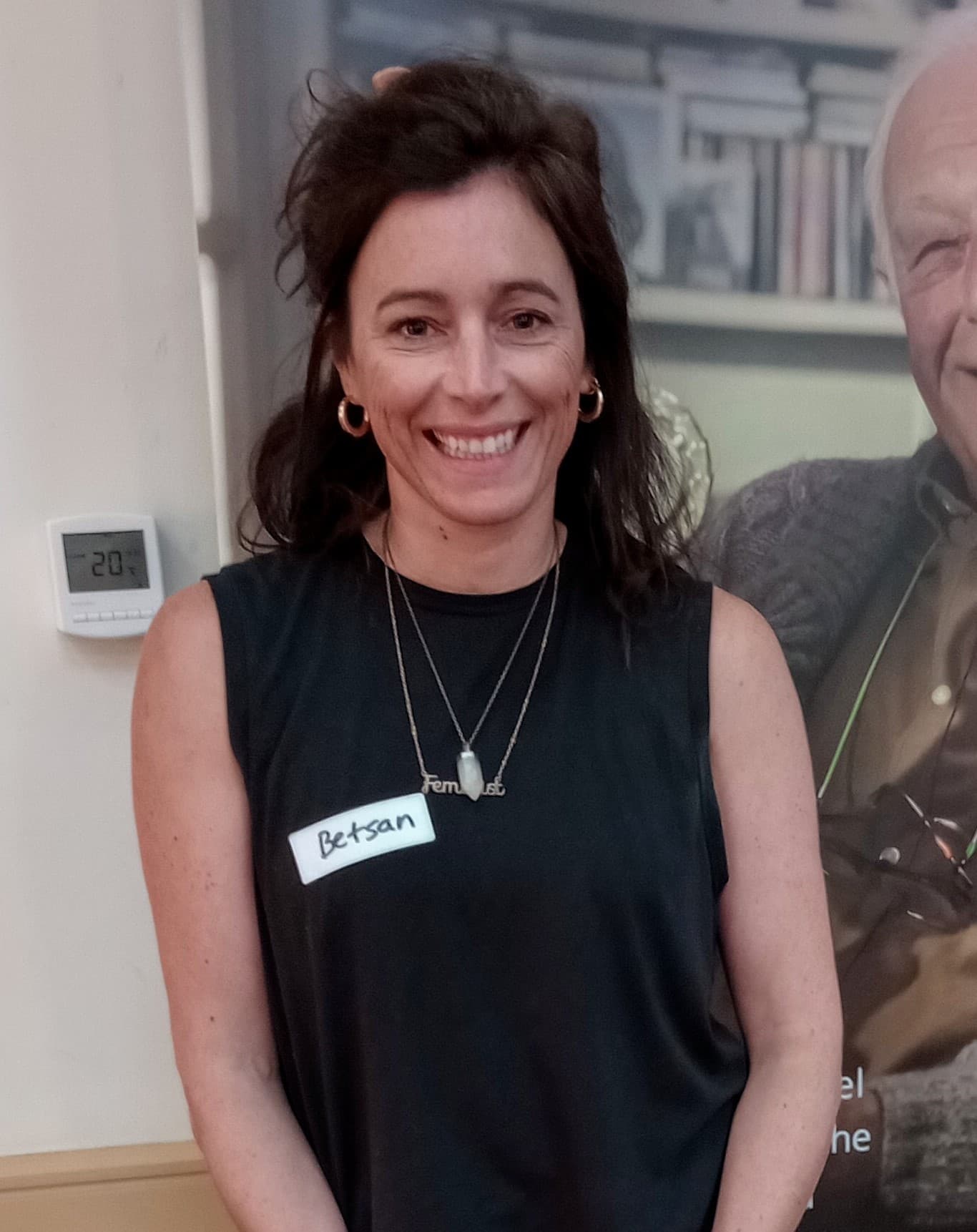 Smiling woman with dark hair in a sleeveless top, wearing a name tag that reads "Betsan. - Home Instead