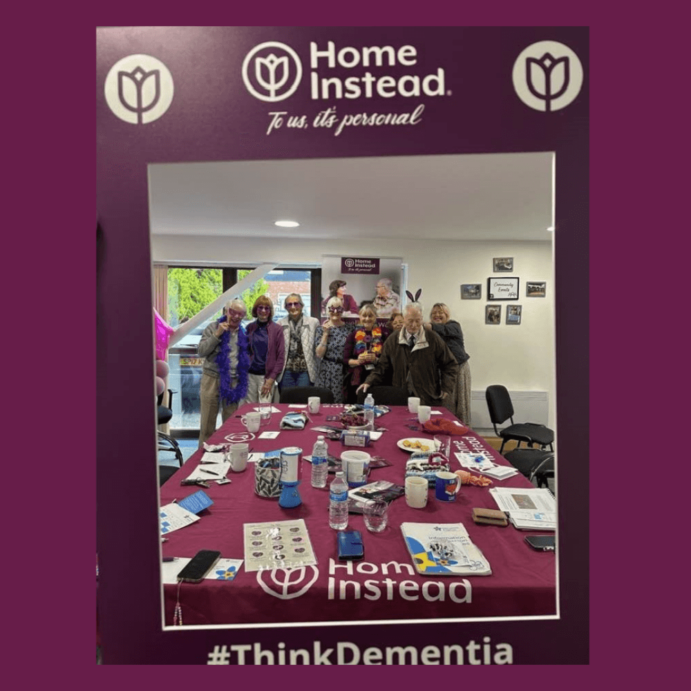 Group of people pose behind a table with dementia awareness materials, framed by a “Home Instead” display. - Home Instead