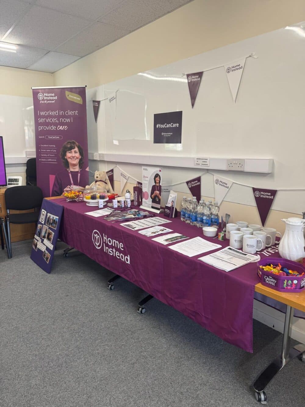 Display table with Home Instead promotional materials and banners in a room. - Home Instead