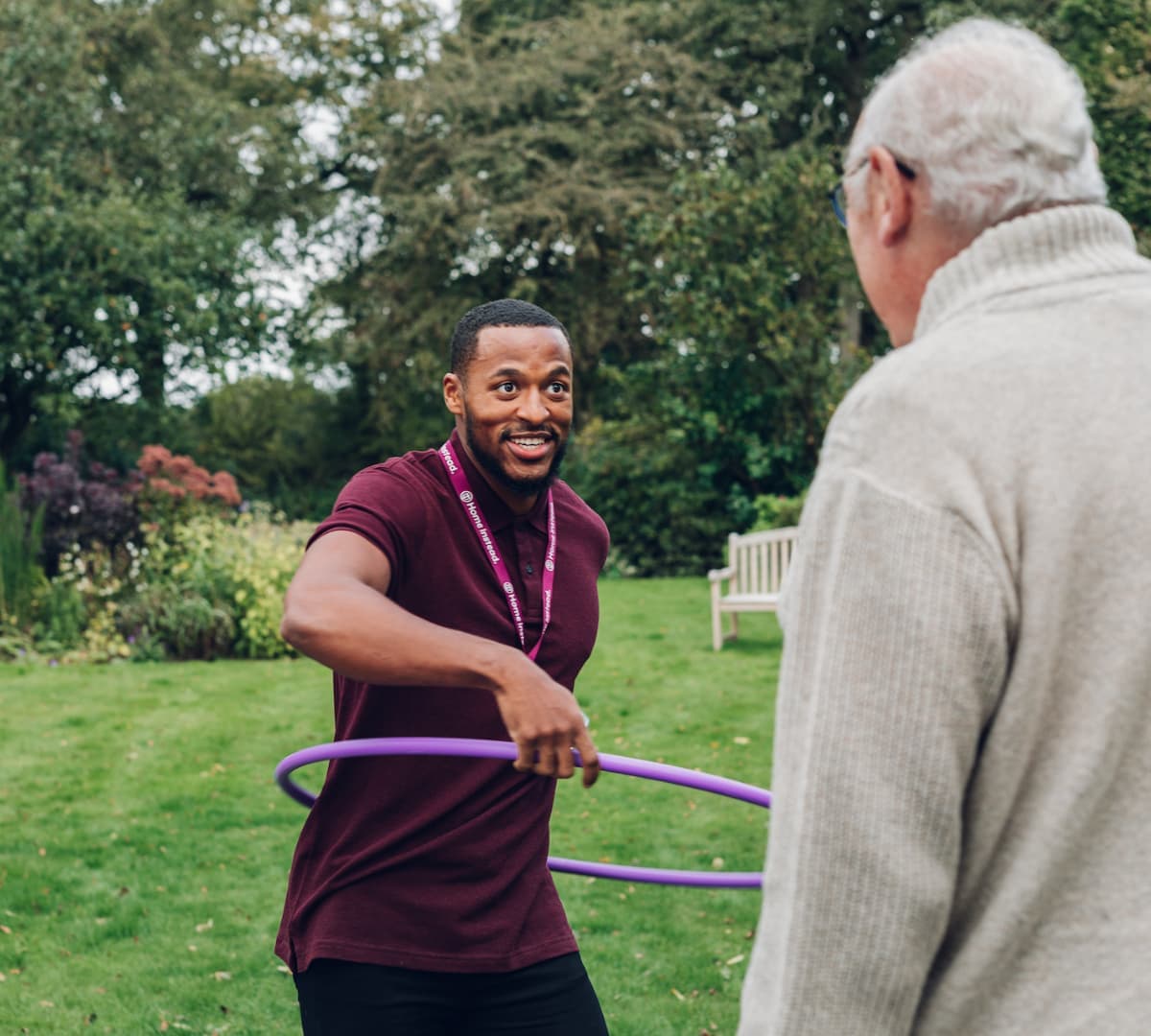 A man playing hula hoop happily in the garden with a senior man