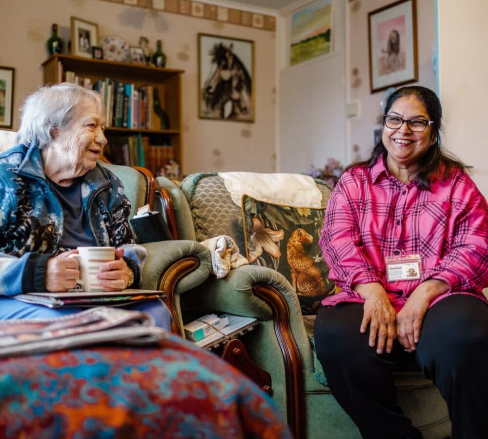 A senior lady with grey hair sitting on a couch while holding a cup with her