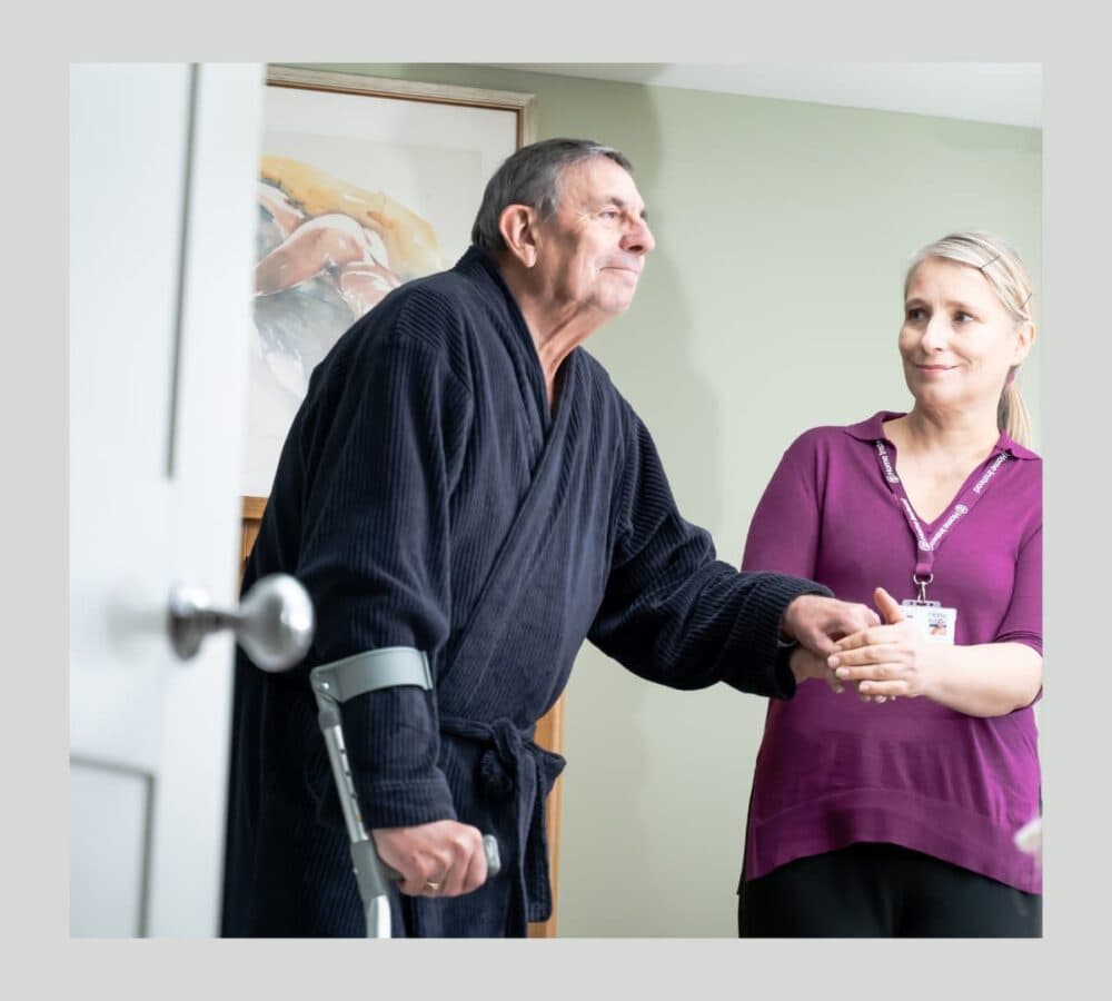 A senior man wearing robe with his carer inside his home