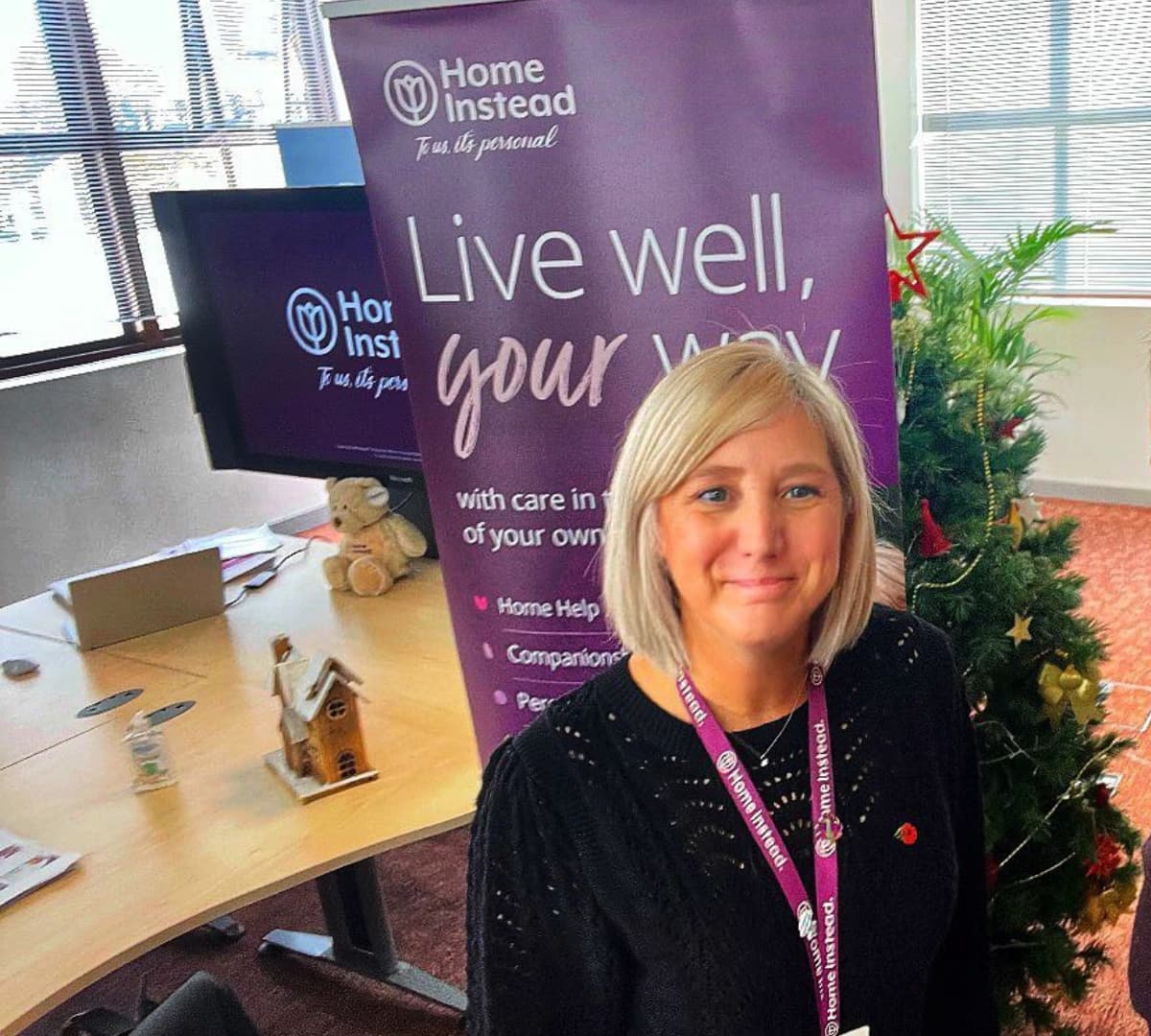 A woman standing with short hair smiling and inside the office with a table and christmas tree at the back