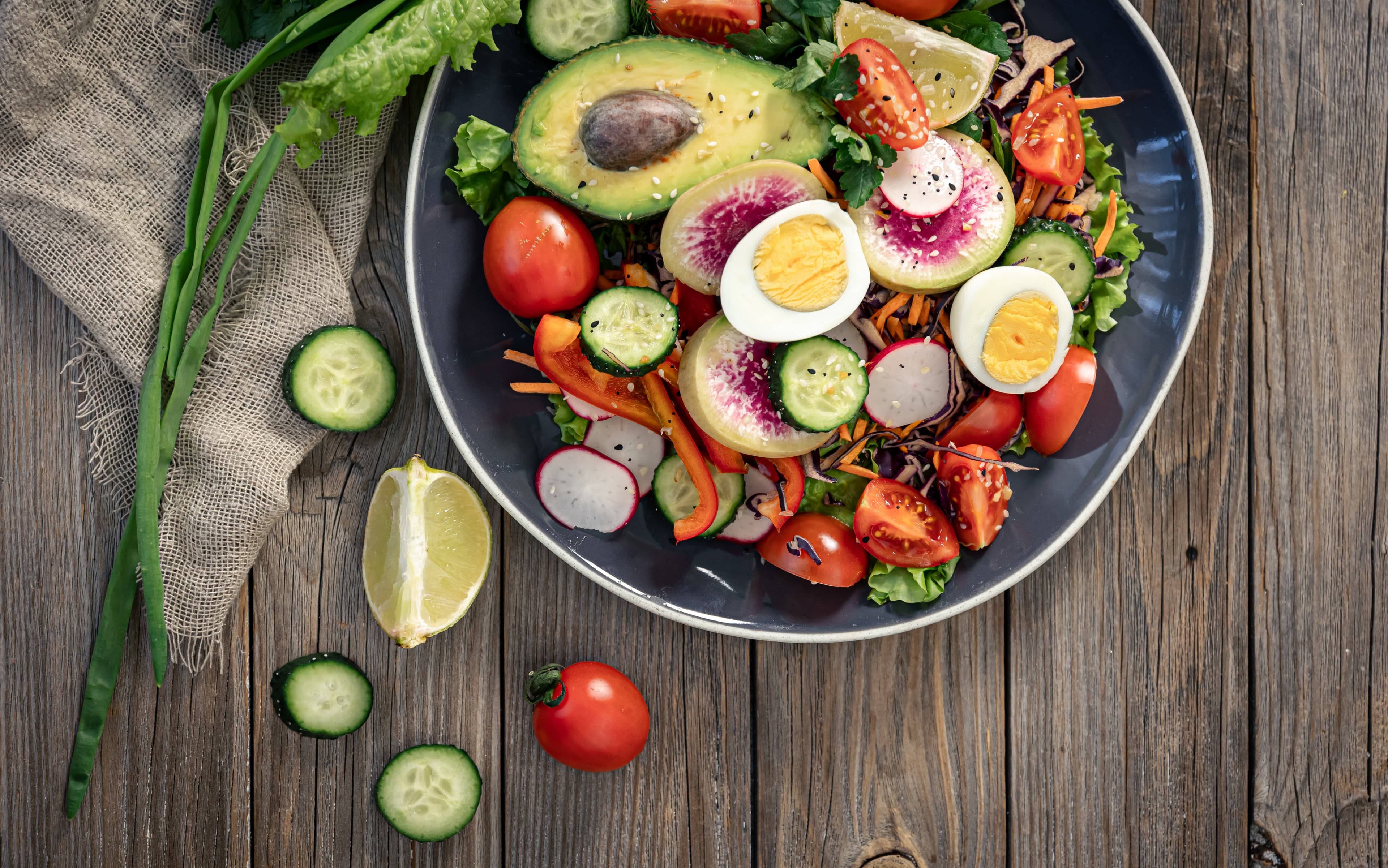 Colorful salad with avocado, boiled eggs, radishes, tomatoes, cucumbers, and greens on a dark plate. - Home Instead