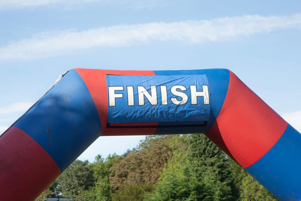 Blue and red inflatable arch with the word "FINISH" stands against a backdrop of trees and a blue sky. - Home Instead
