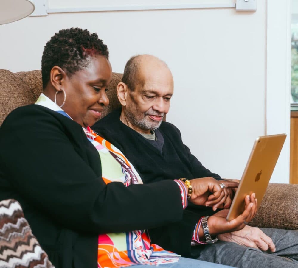 A Home Instead Bournemouth & Christchurch Care Professional with black blazer and holding an iPad while showing something to a client