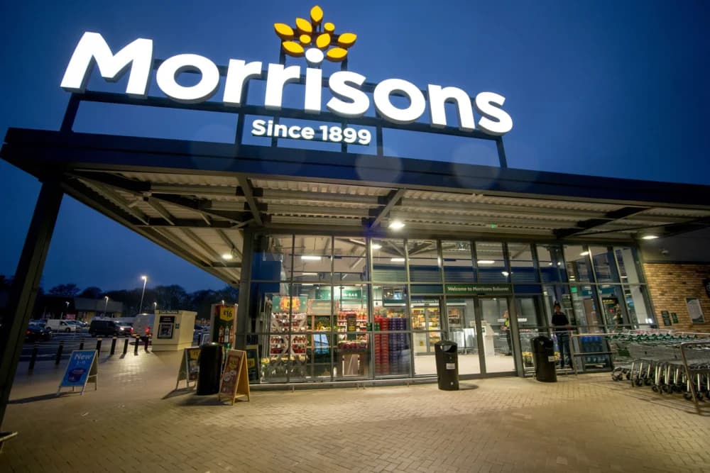 Exterior of a Morrisons supermarket at dusk, with illuminated logo and entrance visible. - Home Instead