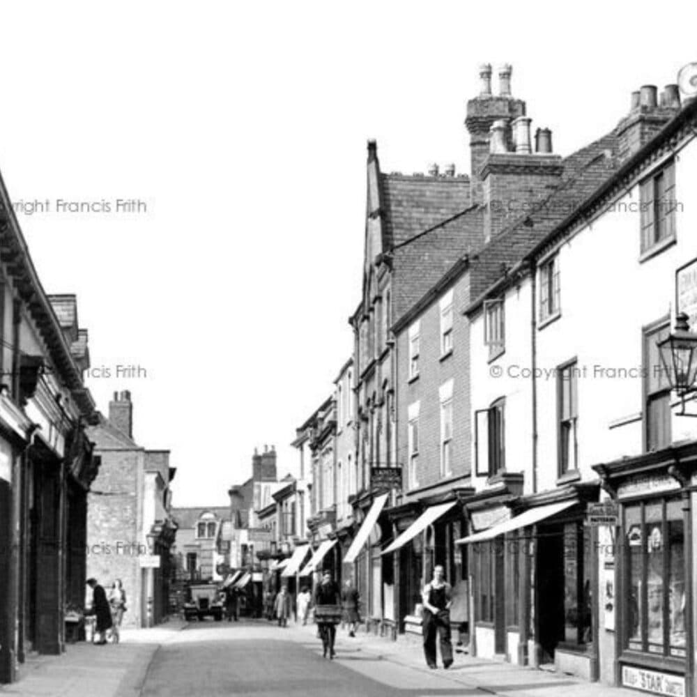 Black and white photo of a vintage street scene with old buildings and people walking. - Home Instead