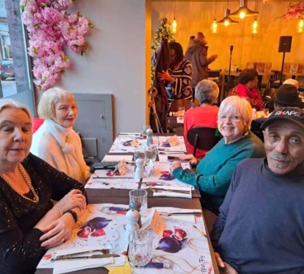 A group of seniors inside a restaurant and sitting on a table, all smiling while waiting for their food.