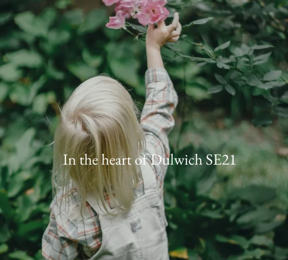 A child with medium length hair looking at a flower and trying to pick it while stretching her hand to reach the flower