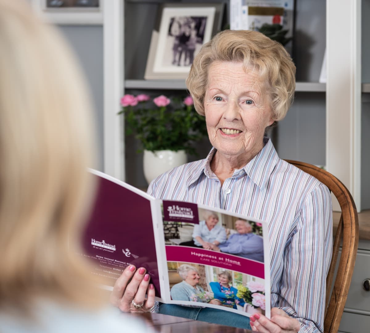 An older woman smiling while reading and discussing about home care with someone inside her home